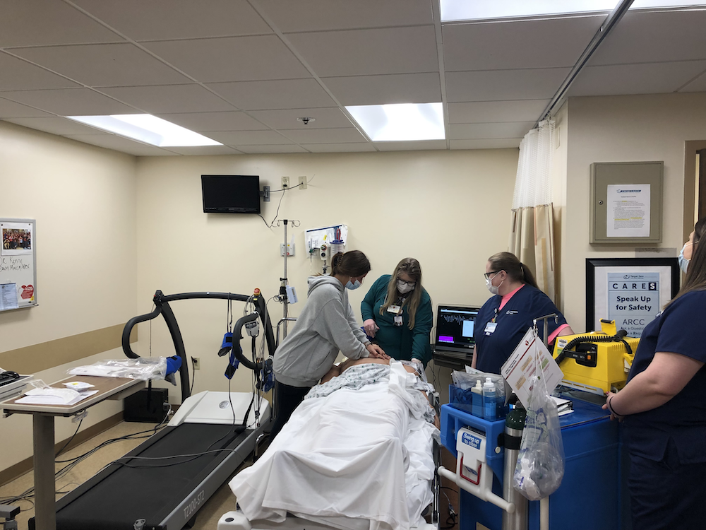 Students in medical masks around a hospital bed shadowing healthcare pros