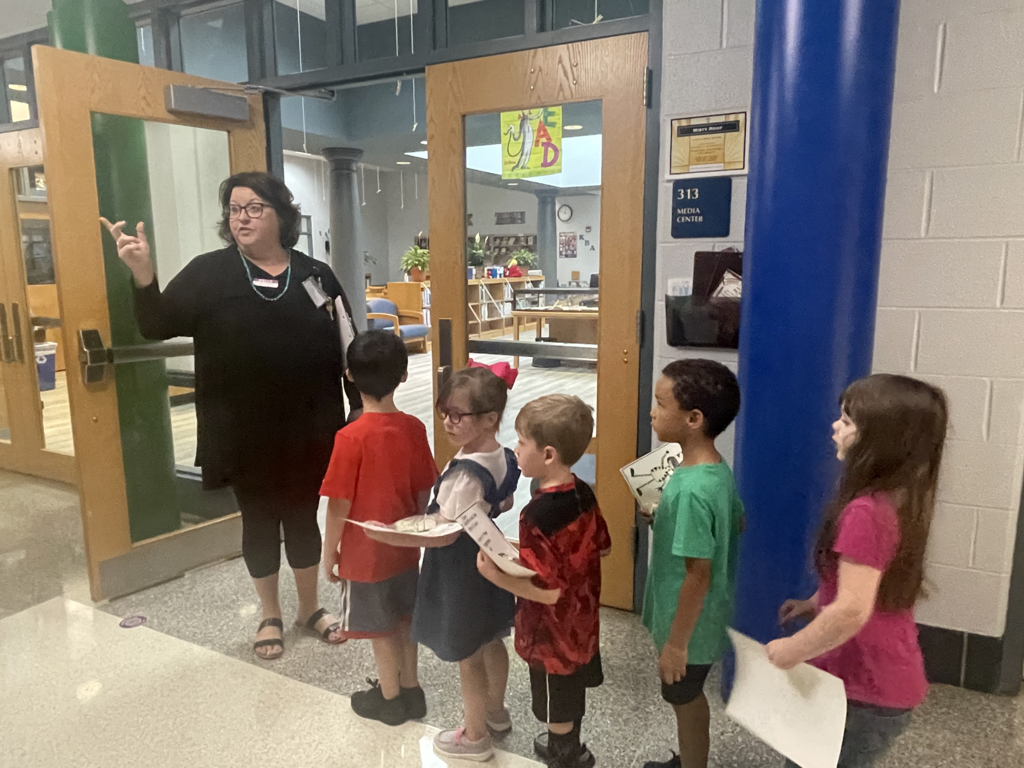 Teacher pointing finger to side in front of lined up kindergartners